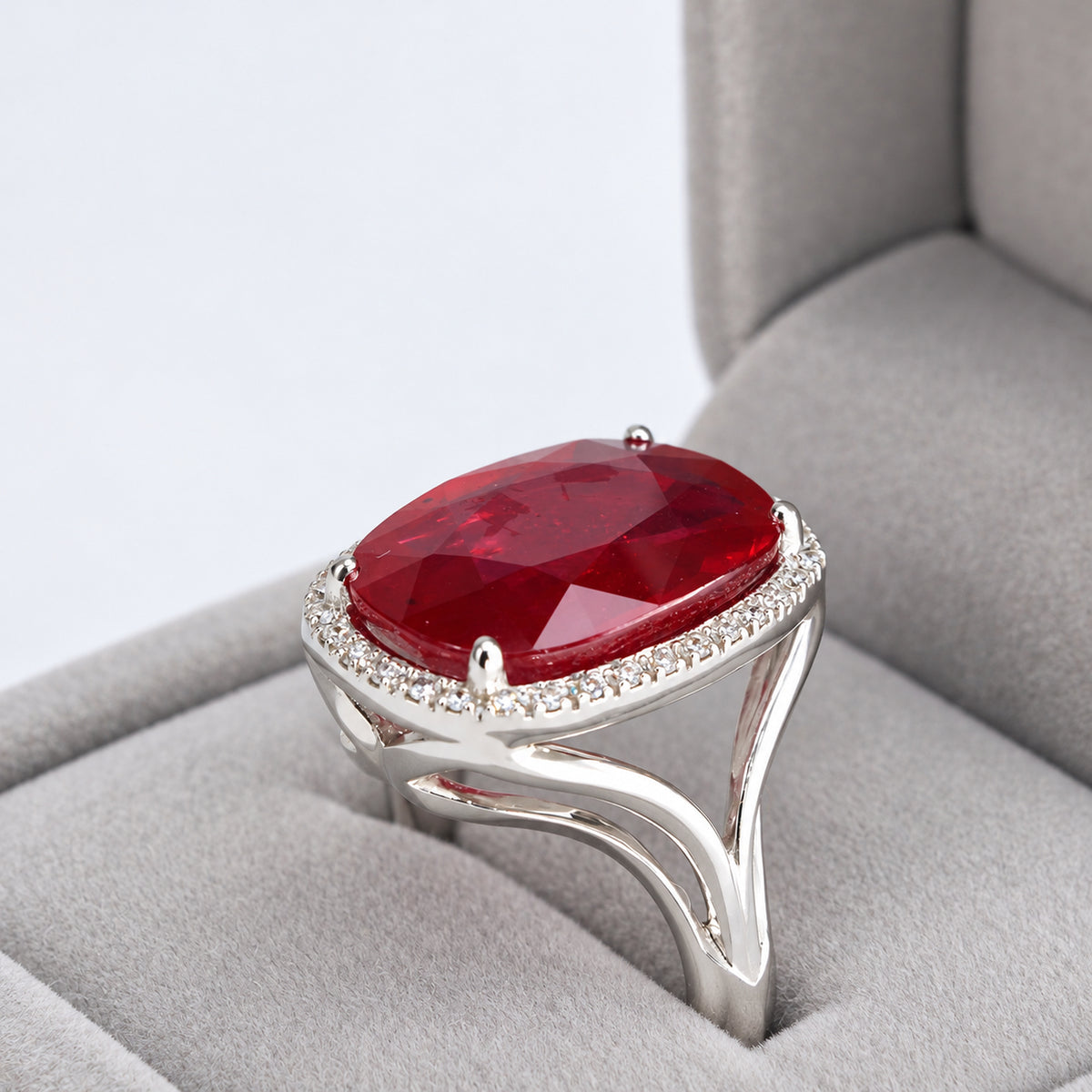 Close-up three-quarter view of 18ct white gold glass-filled ruby and natural diamond halo ring in its box
