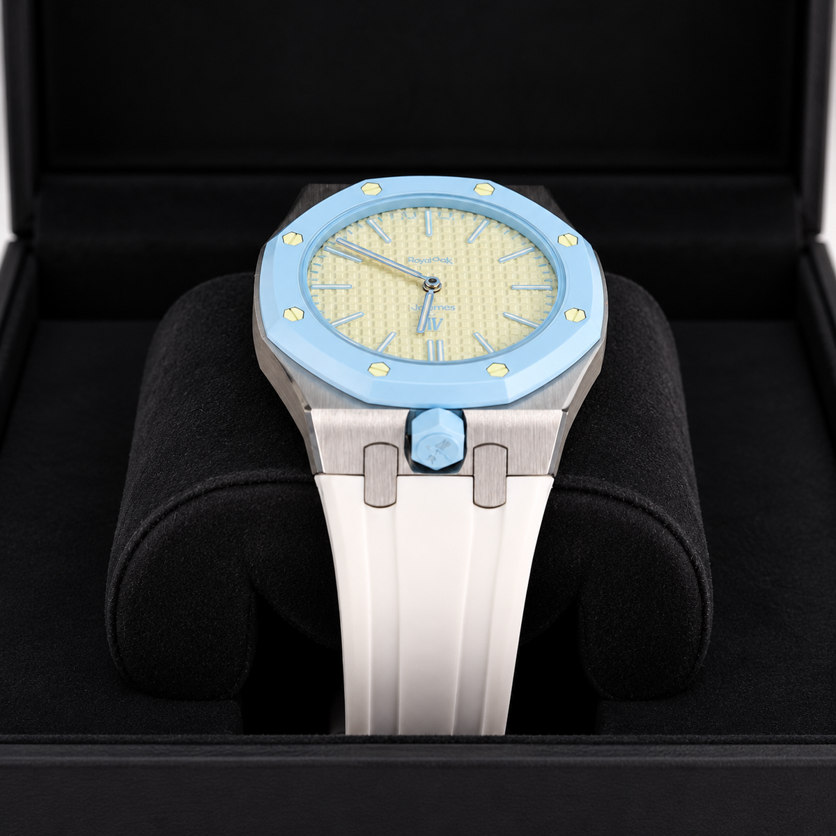A luxury watch with a light blue bezel, a textured pale yellow dial, and a white ceramic strap, presented inside a black watch box.