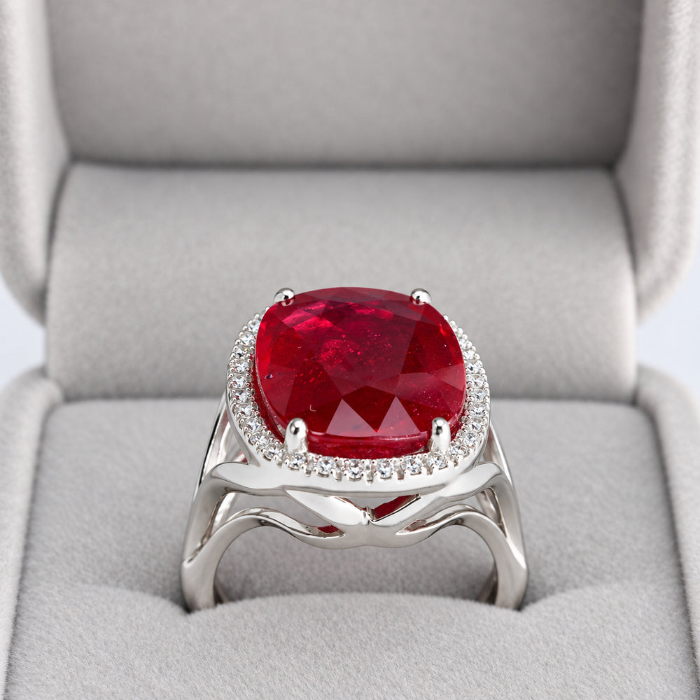 Side view of oval glass-filled ruby and natural diamond halo ring showing open split shoulders in presentation box