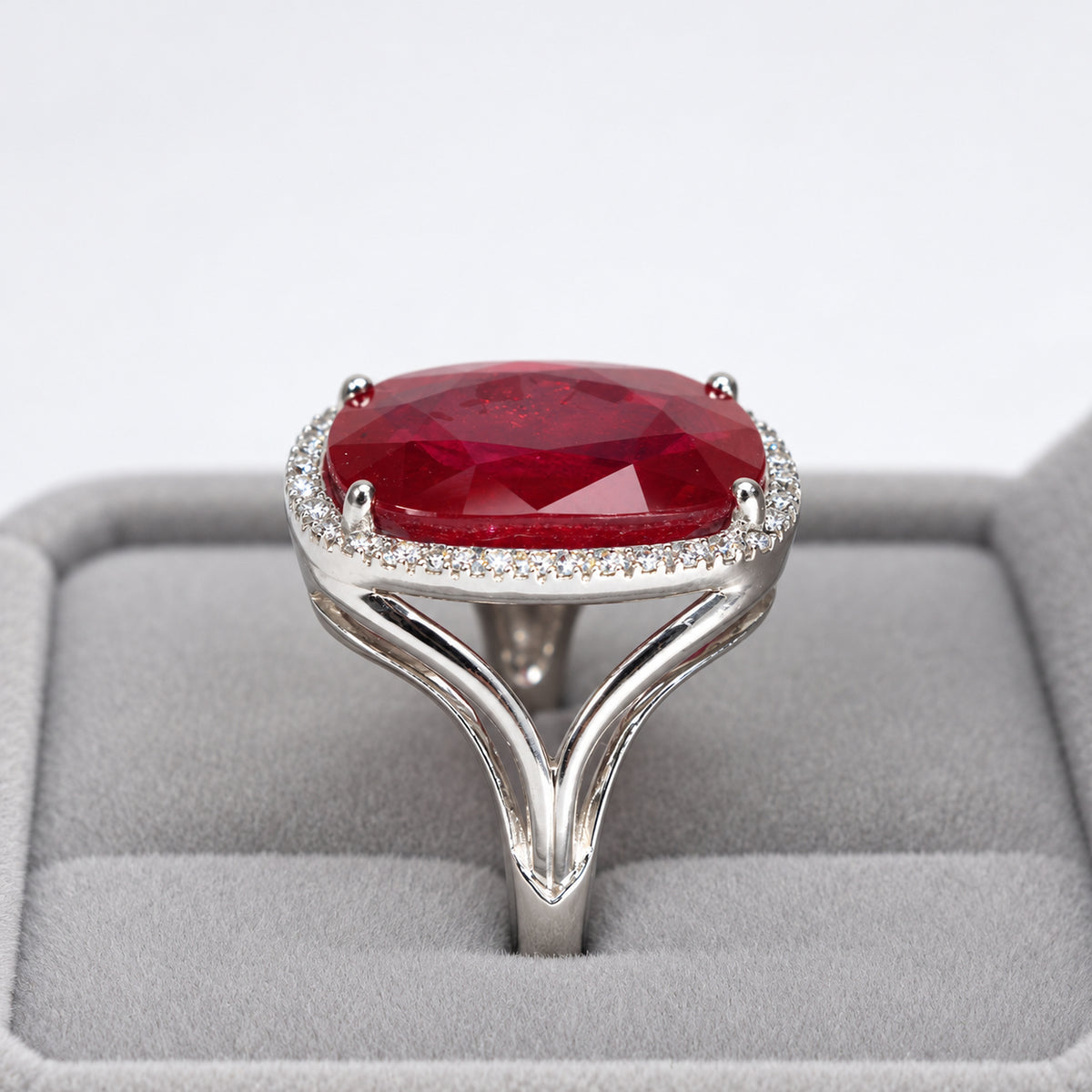 Front profile of oval glass-filled ruby and diamond halo ring displayed in a presentation box