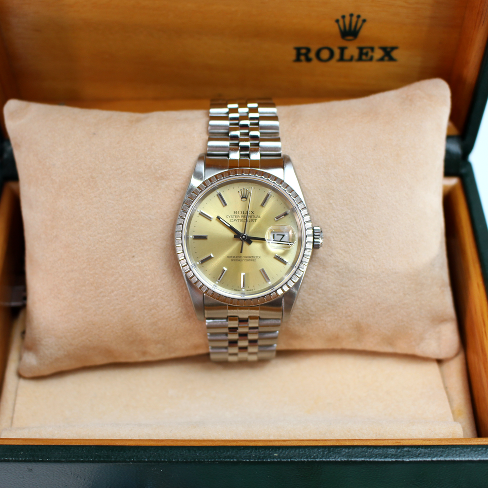 Rolex watch with gold face and silver bracelet on a cushion in a wooden box.