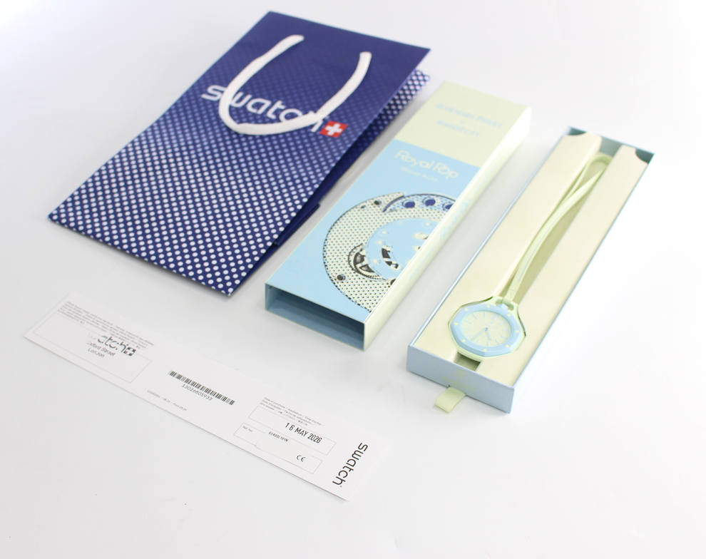 Swatch watch packaging and accessories on a white background, including a blue patterned Swatch shopping bag, a light blue and white Swatch box, a pale green watch strap, and a watch in a pale green presentation box.