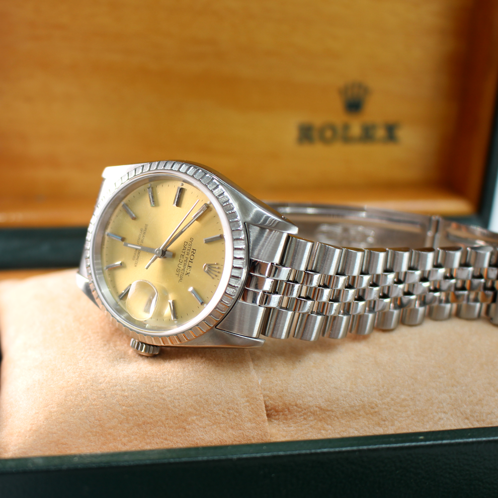 Silver and gold watch on a wooden surface with a blurred Rolex box in the background