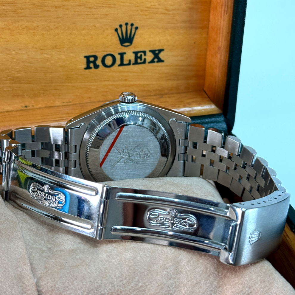 Silver Rolex watch on a light brown surface with a wooden box in the background.