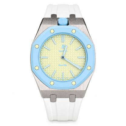A luxury watch featuring a white silicone strap, a brushed stainless steel case, a light blue bezel, and a pale yellow dial with a blue crown.