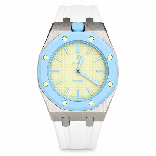 A luxury watch featuring a white silicone strap, a brushed stainless steel case, a light blue bezel, and a pale yellow dial with a blue crown.