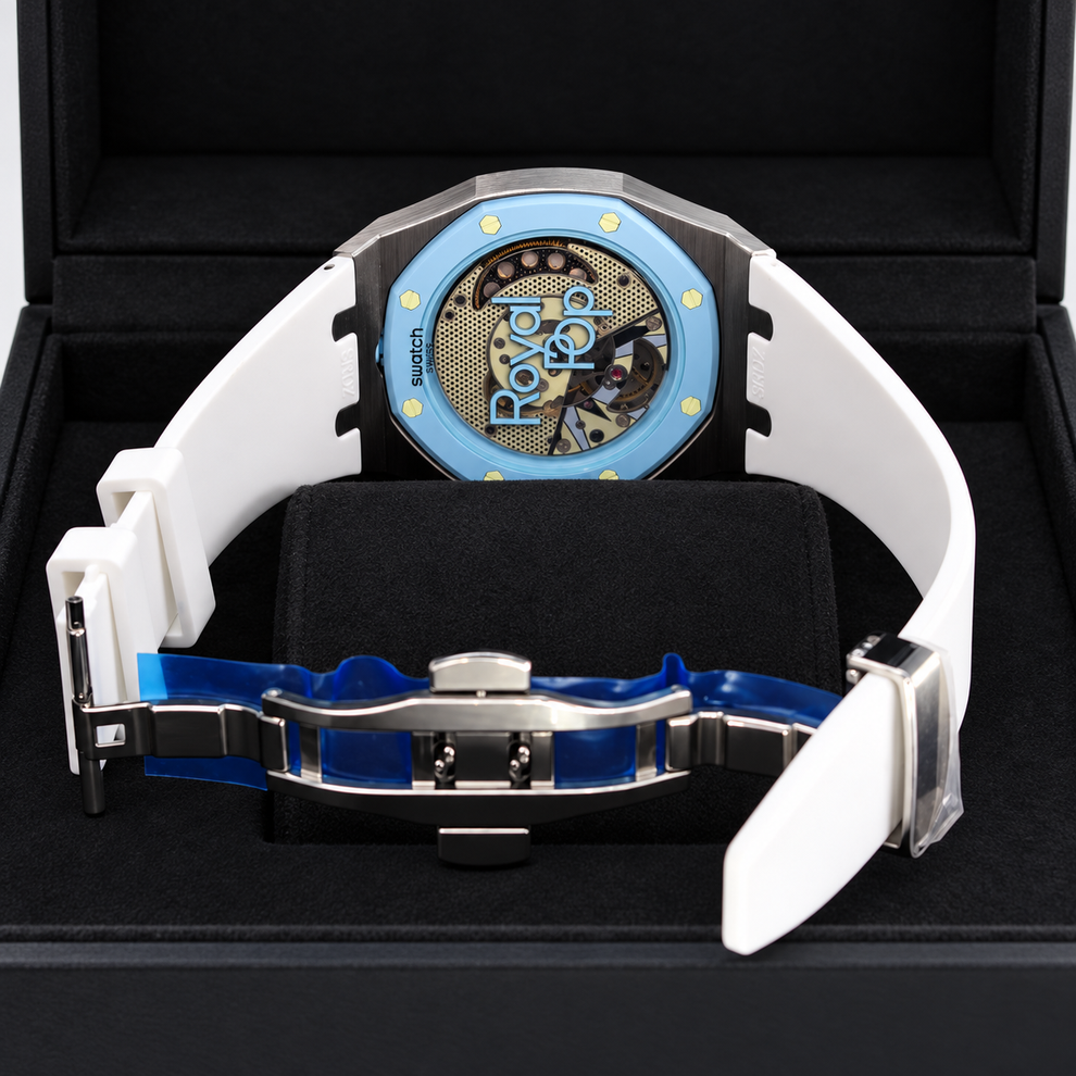 A luxury watch with a white rubber strap, a light blue bezel, and a visible skeleton dial with gold details, presented inside a black watch box.