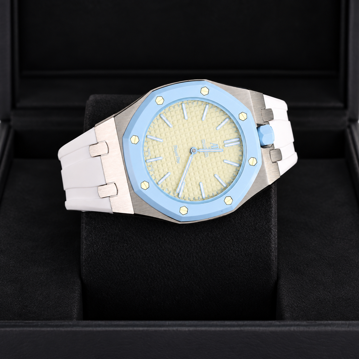 A luxury watch with a light blue bezel, textured cream dial, and white strap, presented inside a black watch box.