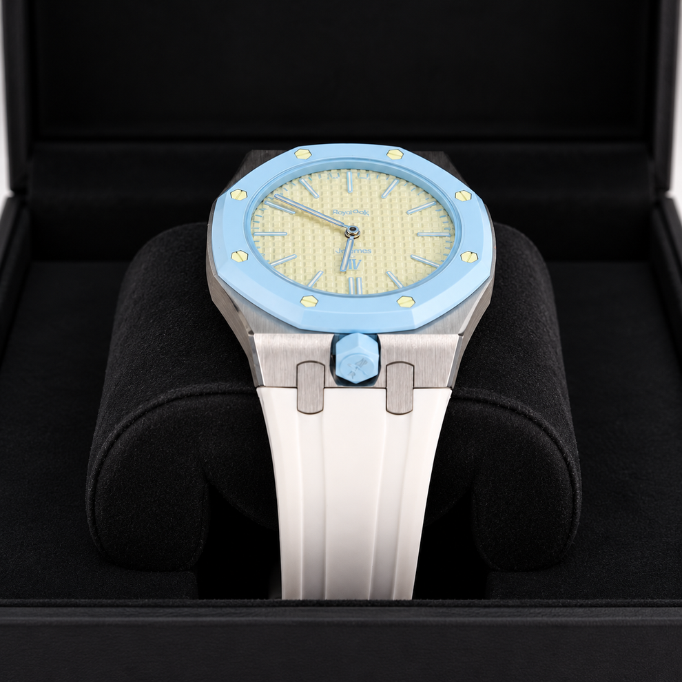 A luxury watch with a light blue bezel, a textured pale yellow dial, and a white ceramic strap, presented inside a black watch box.