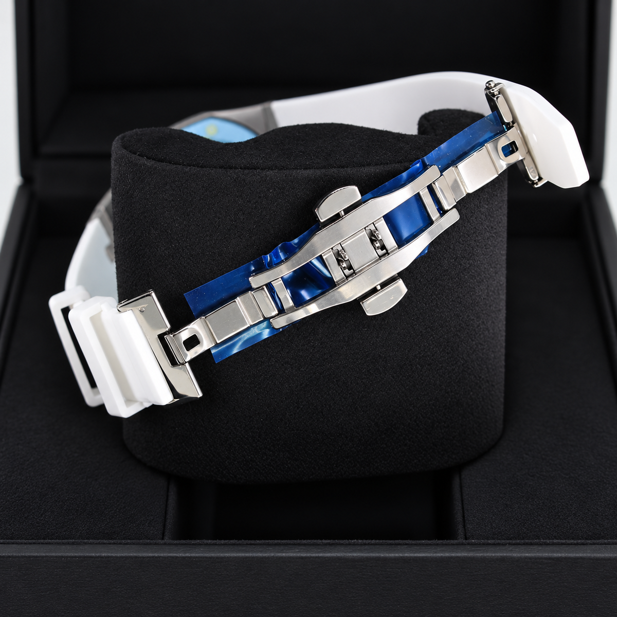 A silver-toned metal bracelet watch with a vibrant blue marbled inlay and a white silicone strap, displayed on a black cushion inside a black watch box.