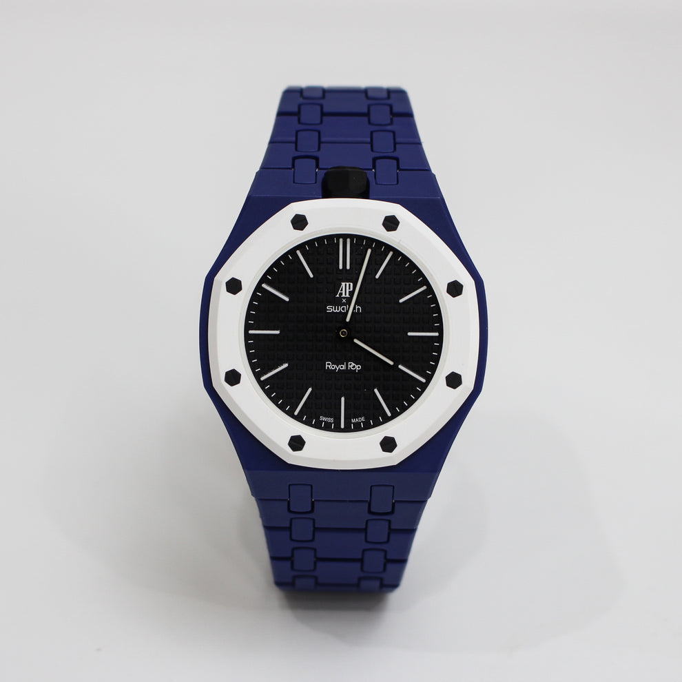 A wristwatch with a dark blue link bracelet, a white bezel, and a black dial, photographed against a light gray background.