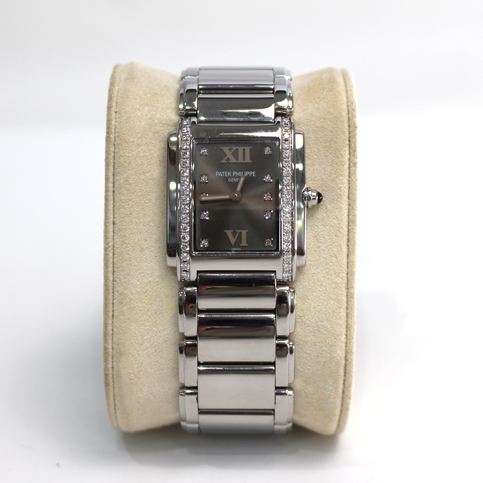 A silver-tone stainless steel wristwatch with a dark gray dial, Roman numeral hour markers, and crystal accents, displayed on a beige cushion.