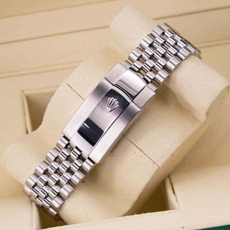 A silver stainless steel watch band with a clasp featuring a crown logo, displayed on a beige watch cushion inside a watch box.
