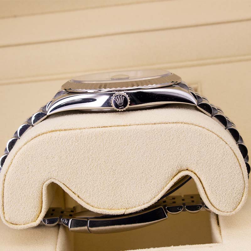 Close-up of a silver-tone metal watch with a textured link bracelet resting on a cream-colored watch cushion inside a watch box.