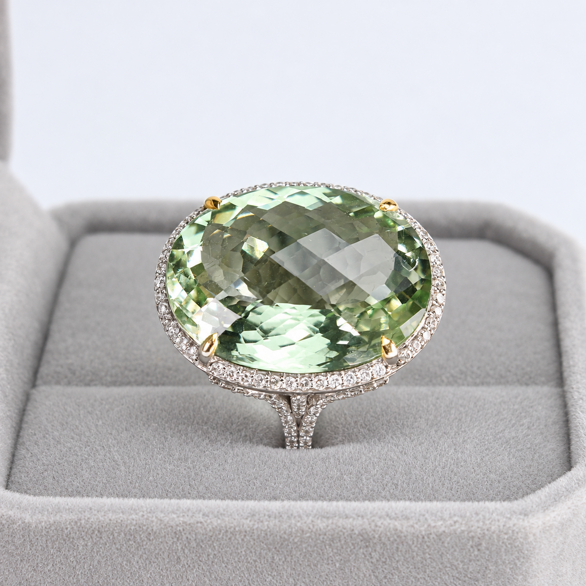 Front view of oval green amethyst and natural diamond halo ring in a grey jewellery presentation box