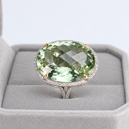 Front view of oval green amethyst and natural diamond halo ring in a grey jewellery presentation box