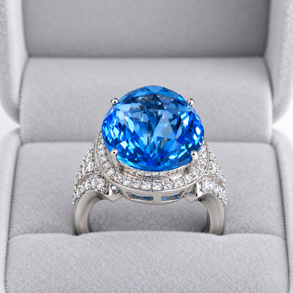 Oval blue topaz and diamond halo cocktail ring displayed in a grey velvet jewellery box.